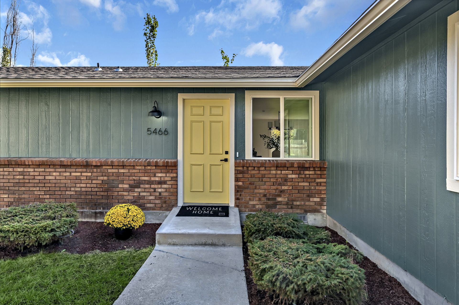 Welcome home mat sits on front step of green house with yellow door