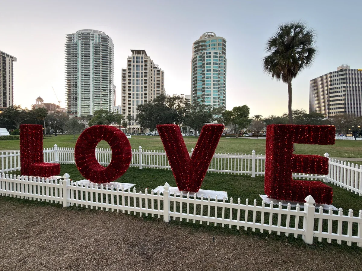 Red LOVE sculpture in a downtown St. Petersburg park with the St. Pete skyline behind it near Beach Drive