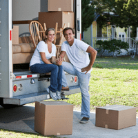 younger couple sitting in the back of a moving truck with boxes around them