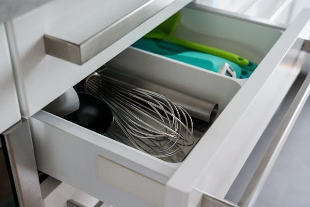 A white kitchen drawer with various utensils.