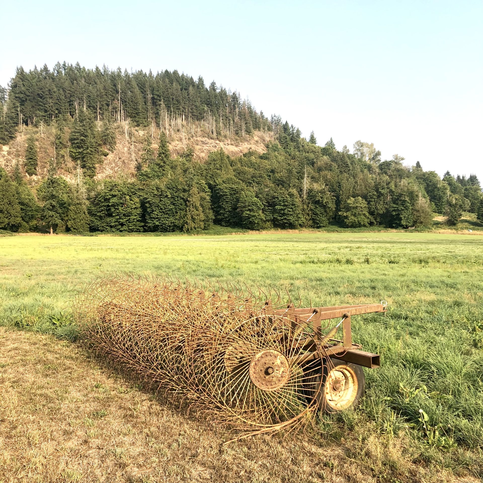 Green field with hill in background and farming equipment in foreground