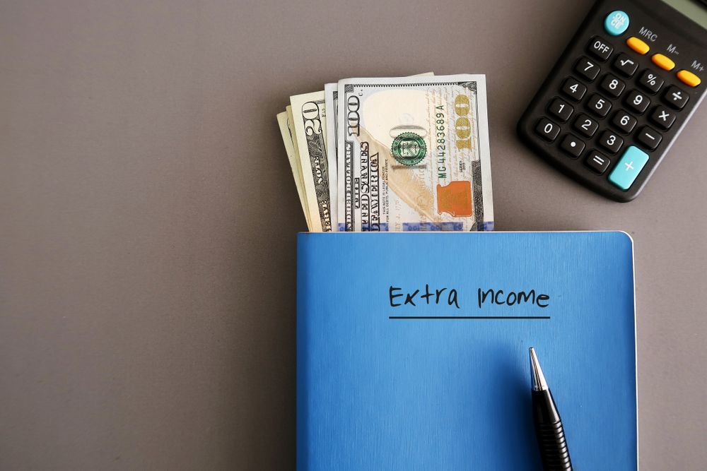 extra-income-written-on-a-blue-book-with-dollar-bills-and-a-calculator extra income written on a blue book with dollar bills and a calculator