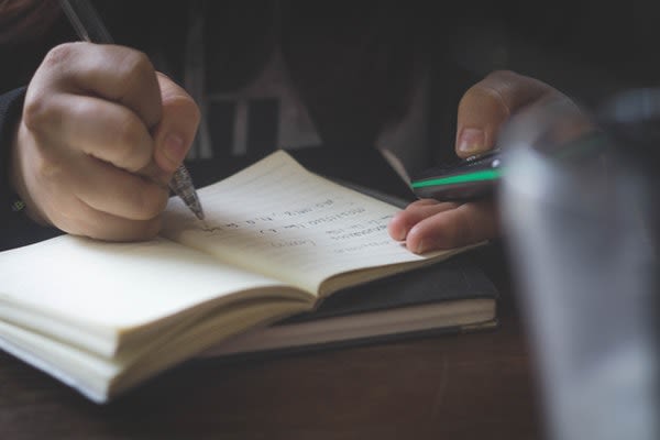Person using phone to research and taking down notes