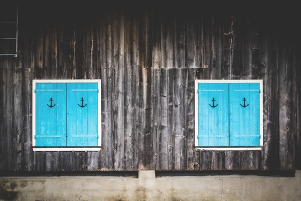 A wall of a home with two windows with turquoise shutters with anchor symbol etched on each
