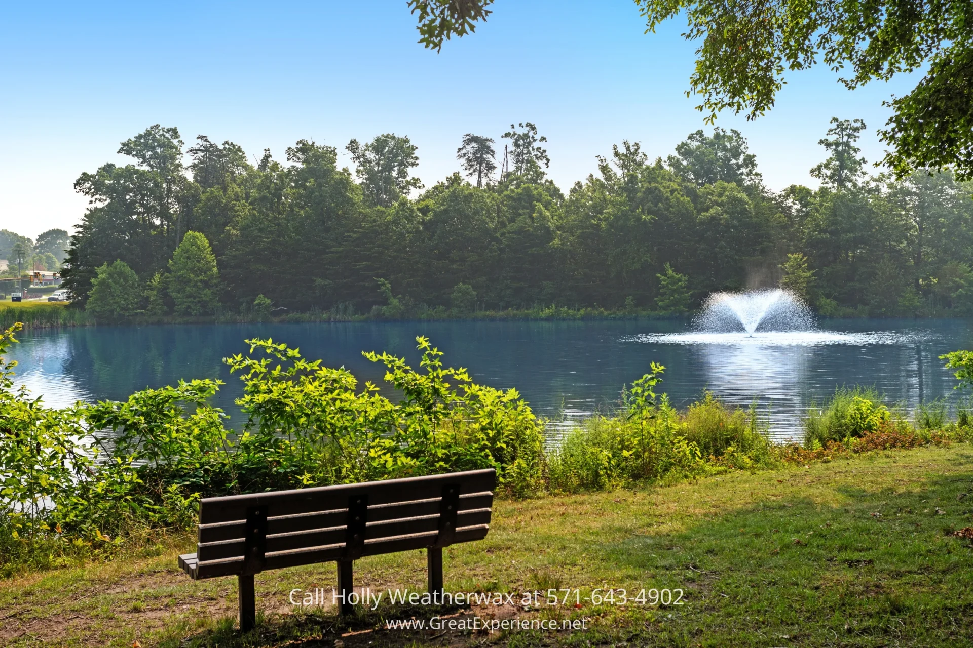 Condo for Sale in Reston VA - Enjoy serene views from your very own balcony when you buy this Reston VA Condo A serene park bench next to a pond with a fountain in the middle, surrounded by trees