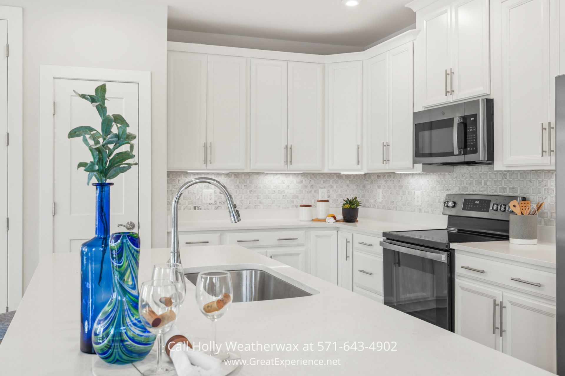 Reston VA Real Estate - Bright white modern kitchen in 1675 Bandit Loop #301B with stainless steel appliances and custom backsplash, near Reston Metro a kitchen with white cabinets and stainless steel appliances