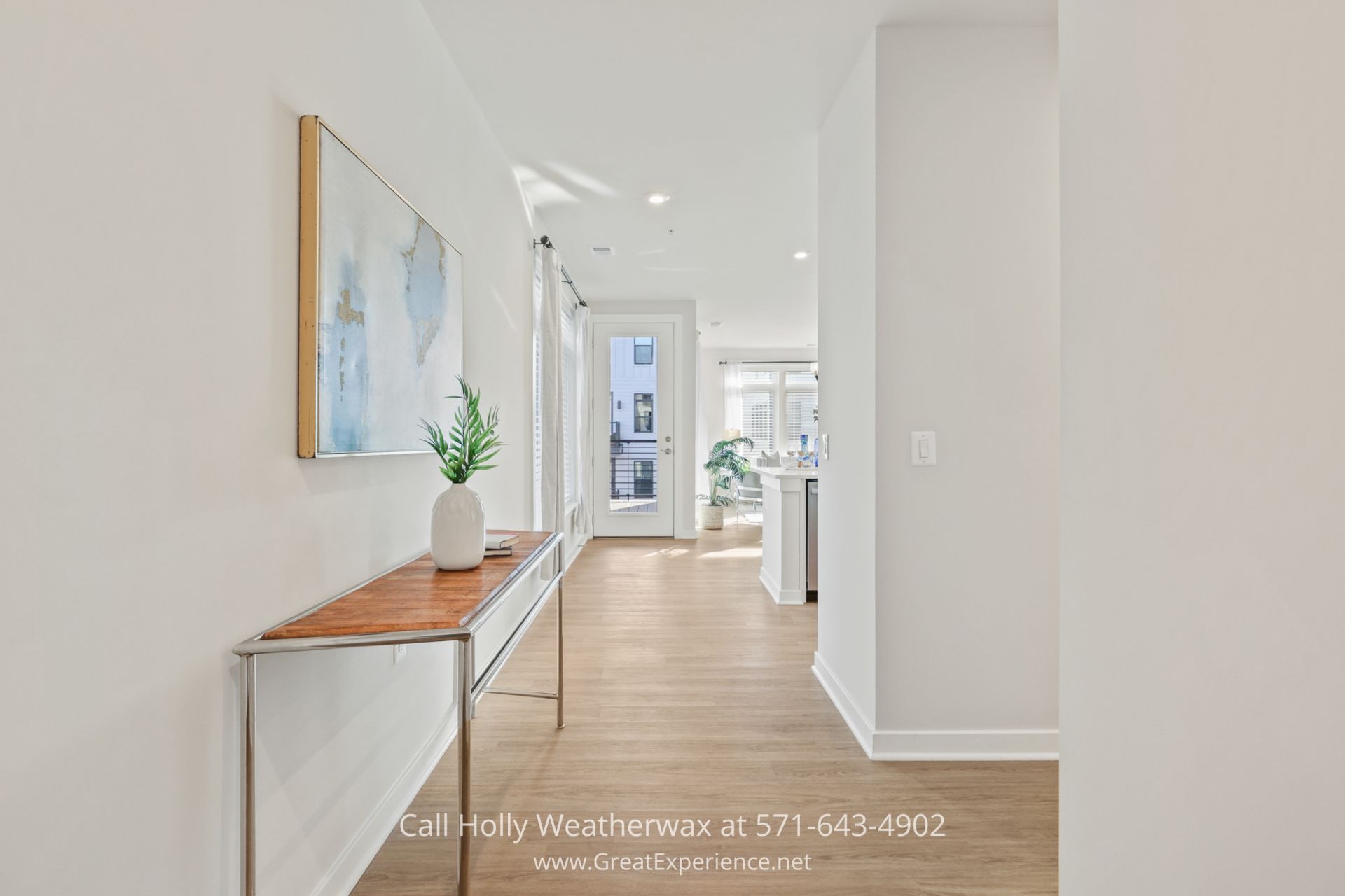 Reston VA Homes - The interior of a condo for sale in Reston VA with neutral colors and custom window treatments located near Dulles Airport a white hallway with a wooden table and a painting on the wall