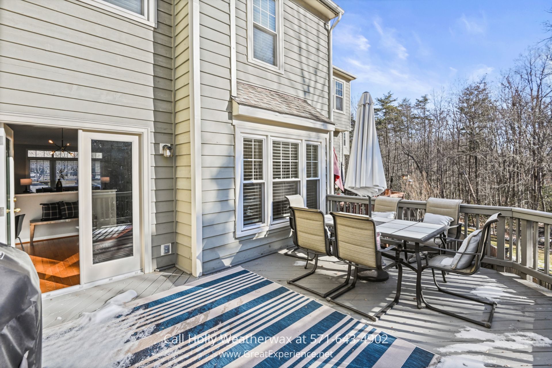 Outdoor Deck with Scenic Views in Reston VA An outdoor deck with a dining table, chairs, and a blue-striped rug, providing a relaxing space with views of nearby trees and a clear blue sky.