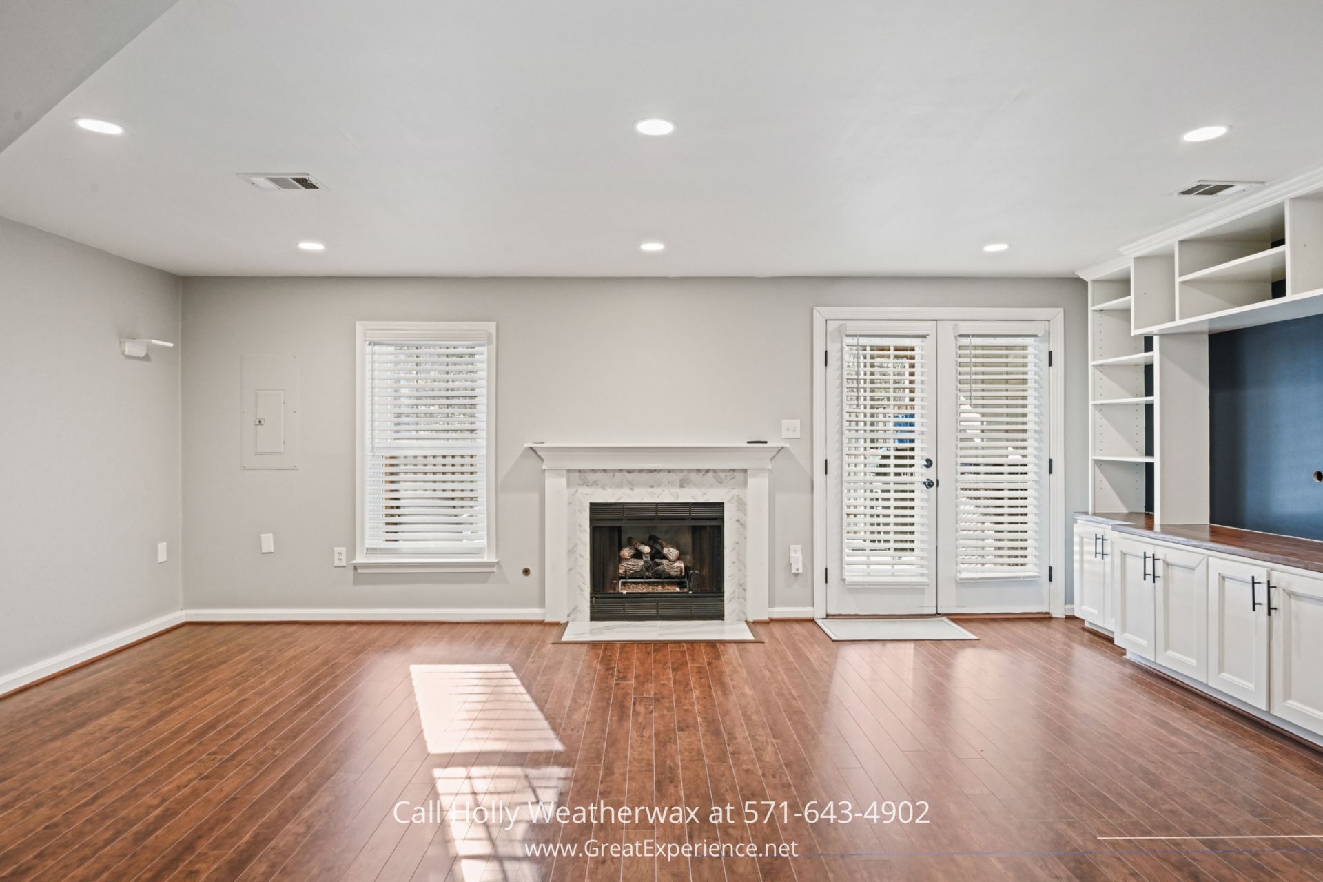 Cozy Family Room in Reston VA Townhouse A bright family room with hardwood flooring, built-in white shelves, a cozy fireplace with a white mantel, and glass doors leading to the outdoor deck.