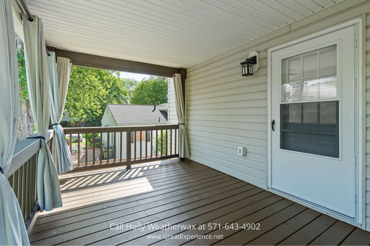 Inviting covered deck with curtains, wooden railings, and views of the backyard in this Chantilly VA home for sale.