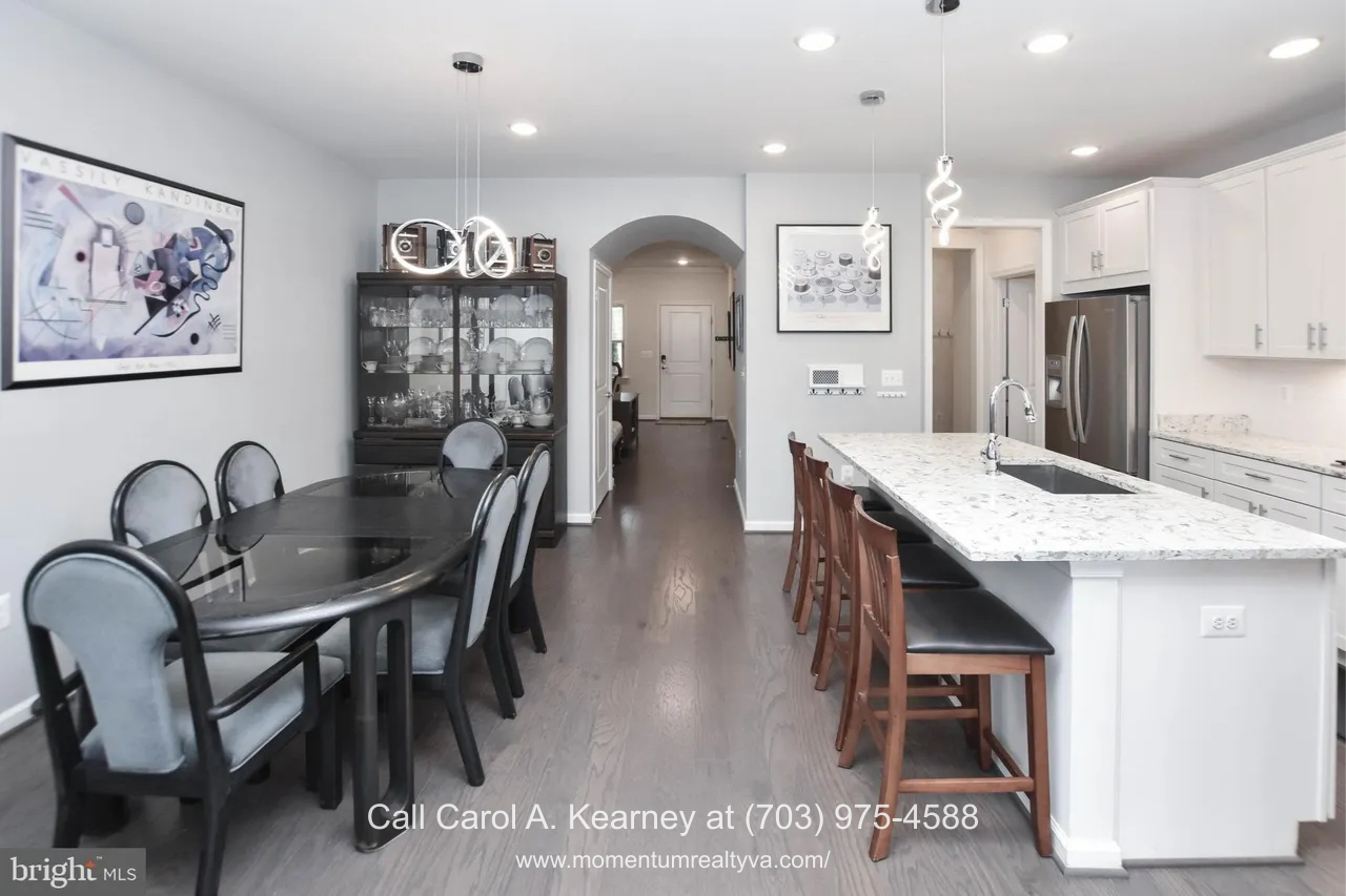 19873 Silvery Blue Ter, Ashburn, VA 20147 Open dining and kitchen area at 19873 Silvery Blue Ter in Ashburn, VA, featuring a quartz island with seating, pendant lighting, stainless steel appliances, hardwood floors, and an open layout ideal for everyday living in the Lexington 7 55+ community.