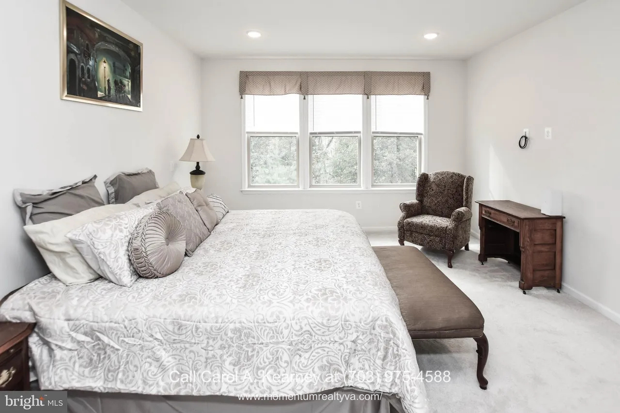 19873 Silvery Blue Ter, Ashburn, VA 20147 Main-level primary bedroom at 19873 Silvery Blue Ter in Ashburn, VA, featuring soft neutral tones, plush carpeting, large windows with wooded views, and a spacious layout designed for comfortable one-level living in the Lexington 7 55+ community.