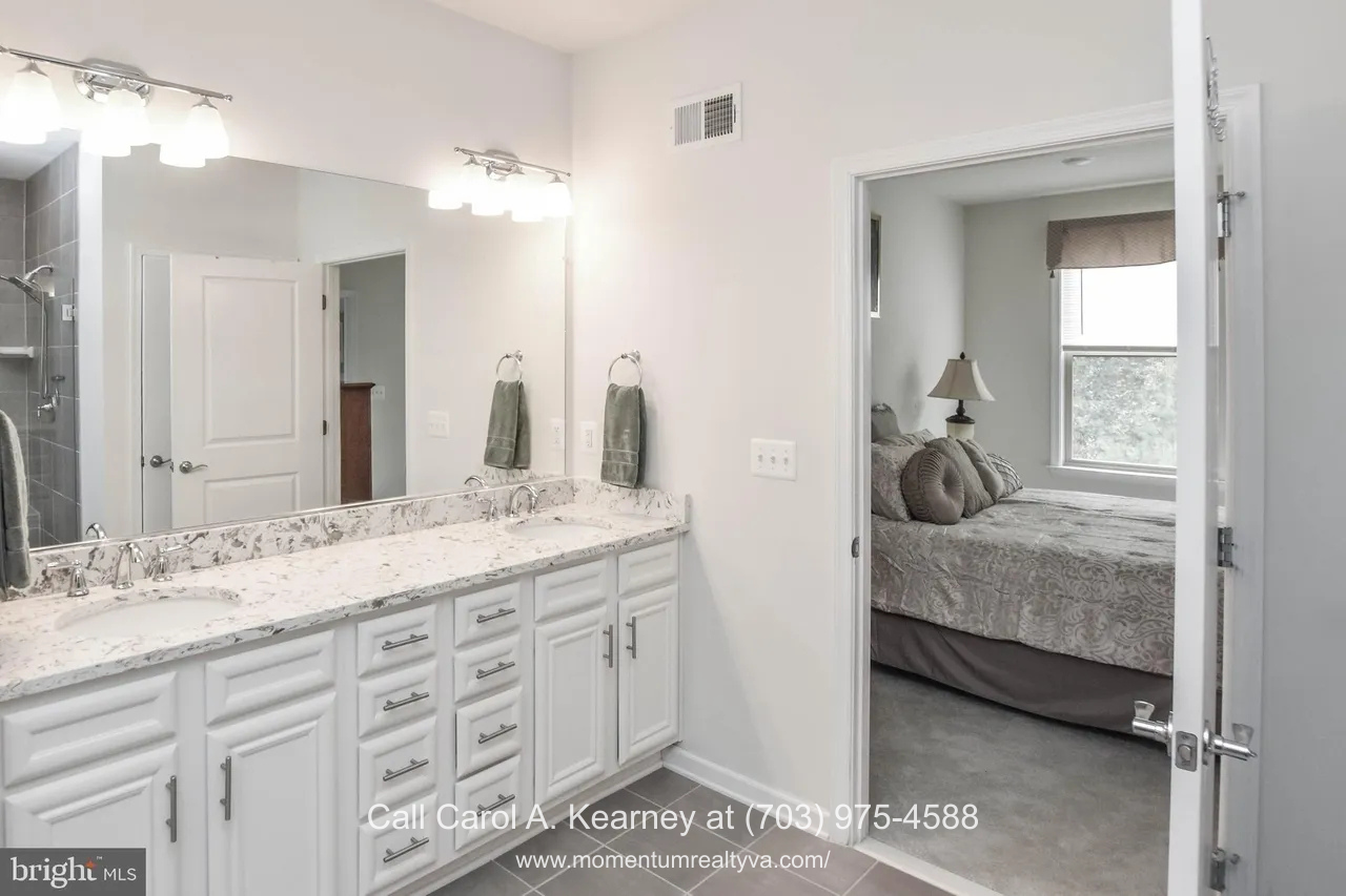 19873 Silvery Blue Ter, Ashburn, VA 20147 Main-level primary bathroom at 19873 Silvery Blue Ter in Ashburn, VA, featuring a double vanity with quartz countertops, white cabinetry, large mirror, modern lighting, and direct access to the primary bedroom in the Lexington 7 55+ community.