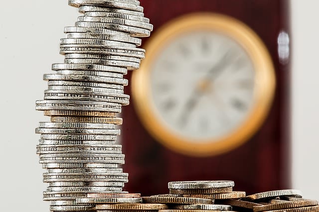 A stack of money sitting on a table with a clock in the background