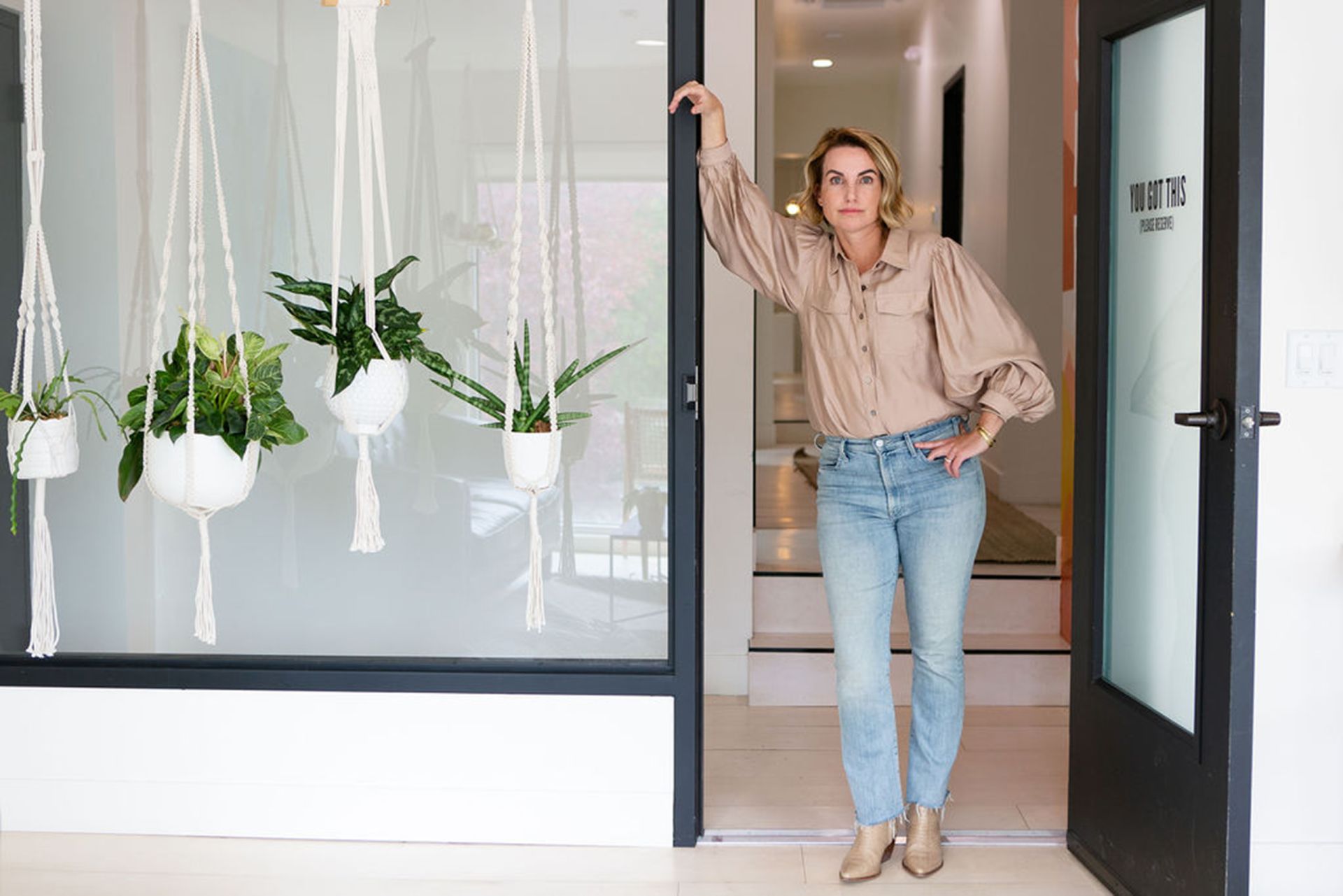 how to start a small business in Salt Lake City an attractive middle aged blonde woman stands in the doorway of an inviting office space with a glass door and hanging house plants