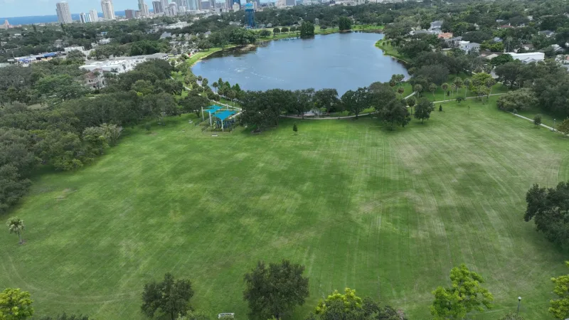 Aerial view of Crescent Lake Park in St. Petersburg, Florida, showing the lake, open green space, trees, and downtown skyline in the background.