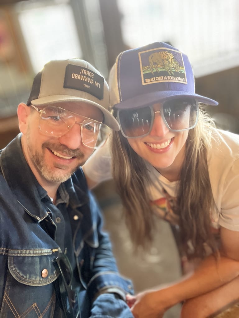 Sean and Steavy wearing trucker hats and big sunglasses, laughing together — playful and candid.