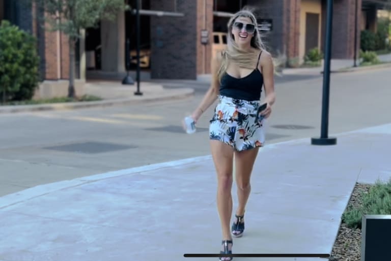 Steavy Carter walking down a colorful urban street in denim shorts and a low-cut black top — a casual and stylish lifestyle photo.