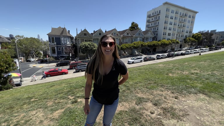 Steavy Carter wearing jeans, a black top, and big sunglasses, posing confidently near the Painted Ladies — city-chic branding.