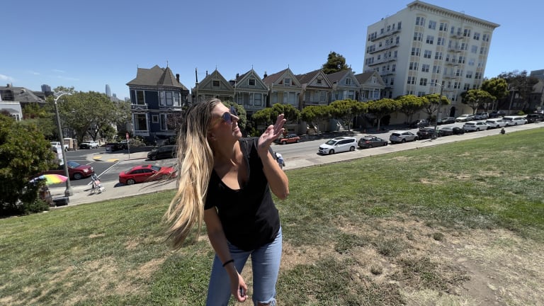 Steavy Carter in front of the Painted Ladies in San Francisco, gesturing playfully — travel-inspired lifestyle branding.
