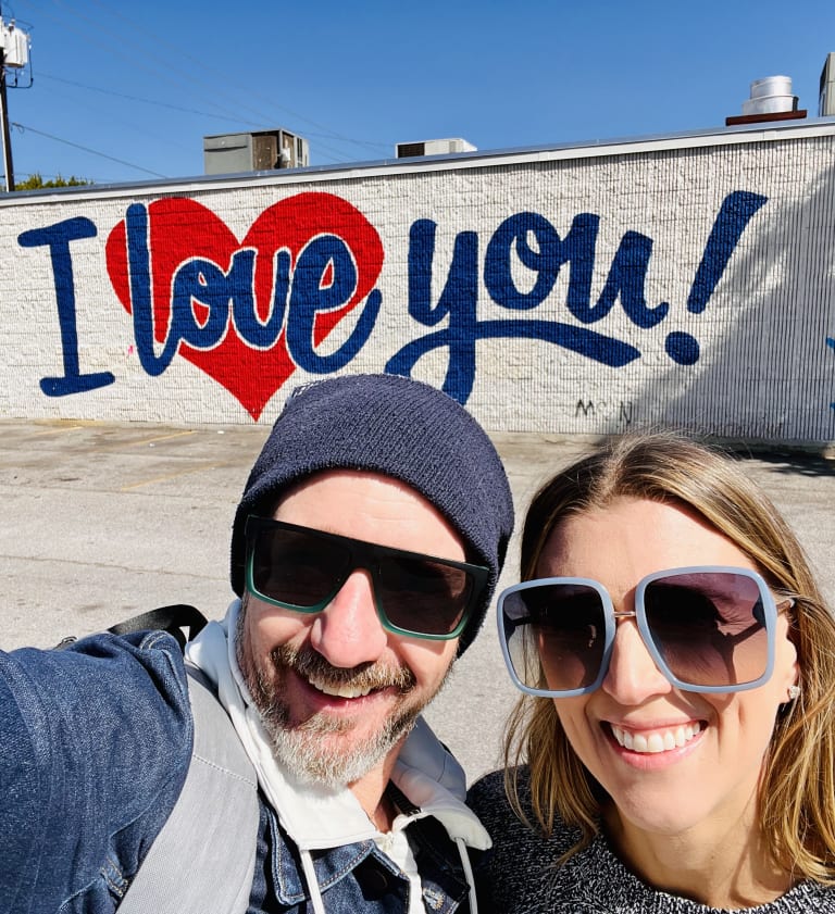 Sean and Steavy Carter in front of the 'I Love You' mural — Sean in a beanie, Steavy wearing bold square sunglasses.