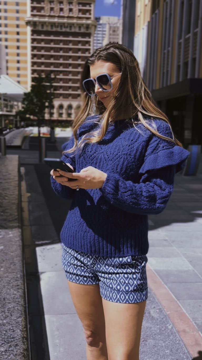 Steavy Carter texting while wearing a blue sweater and shorts in the AT&T Discovery District — downtown Dallas lifestyle.