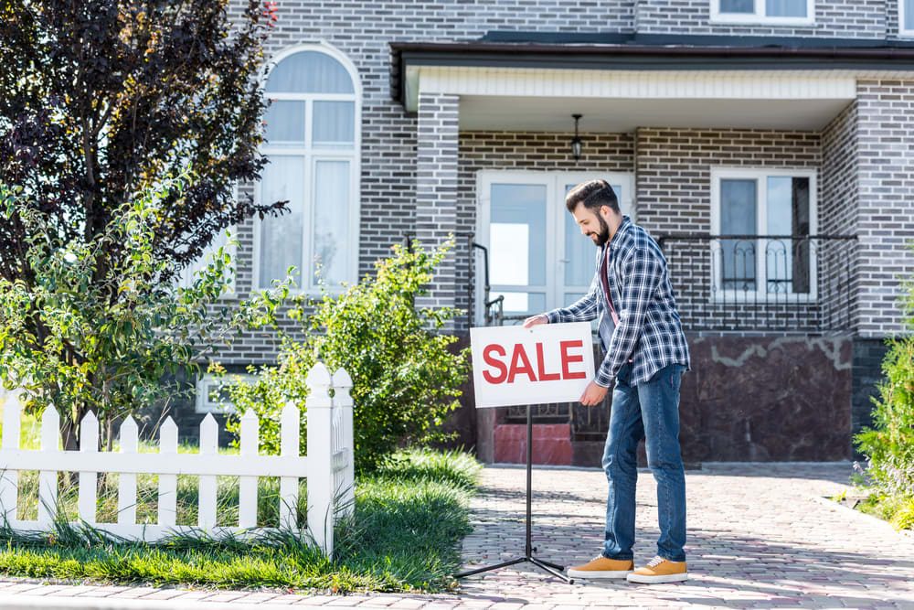 A homeowner placing a for-sale sign in the yard