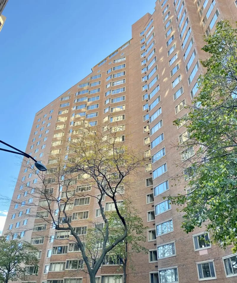 Red brick high-rise condominium with sawtooth oriel windows on Lake Shore Drive in Chicago's Gold Coast, framed by trees