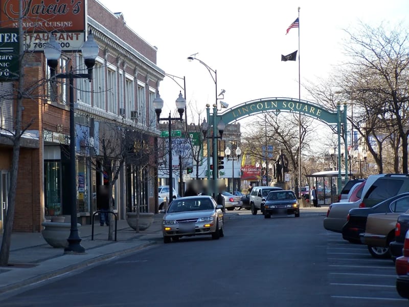 Green Lincoln Square arch over a street lined with brick storefronts and lampposts in Chicago's Lincoln Square