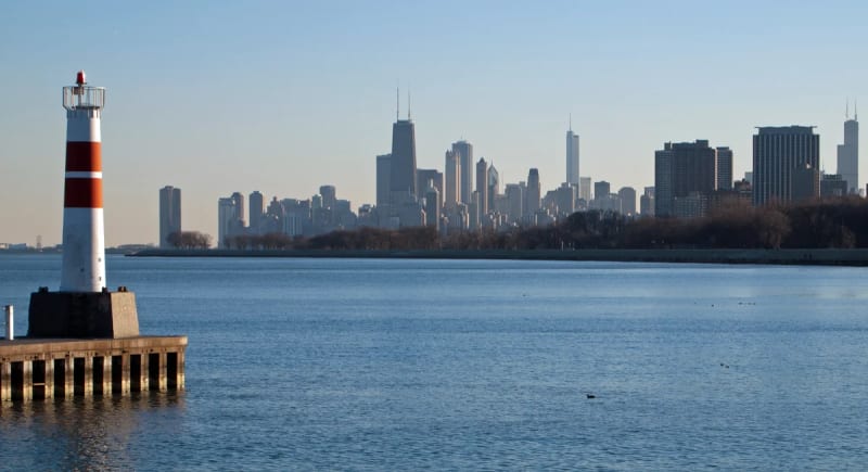 Red-and-white lighthouse at Montrose Harbor with the Chicago skyline across Lake Michigan on a clear late-fall day